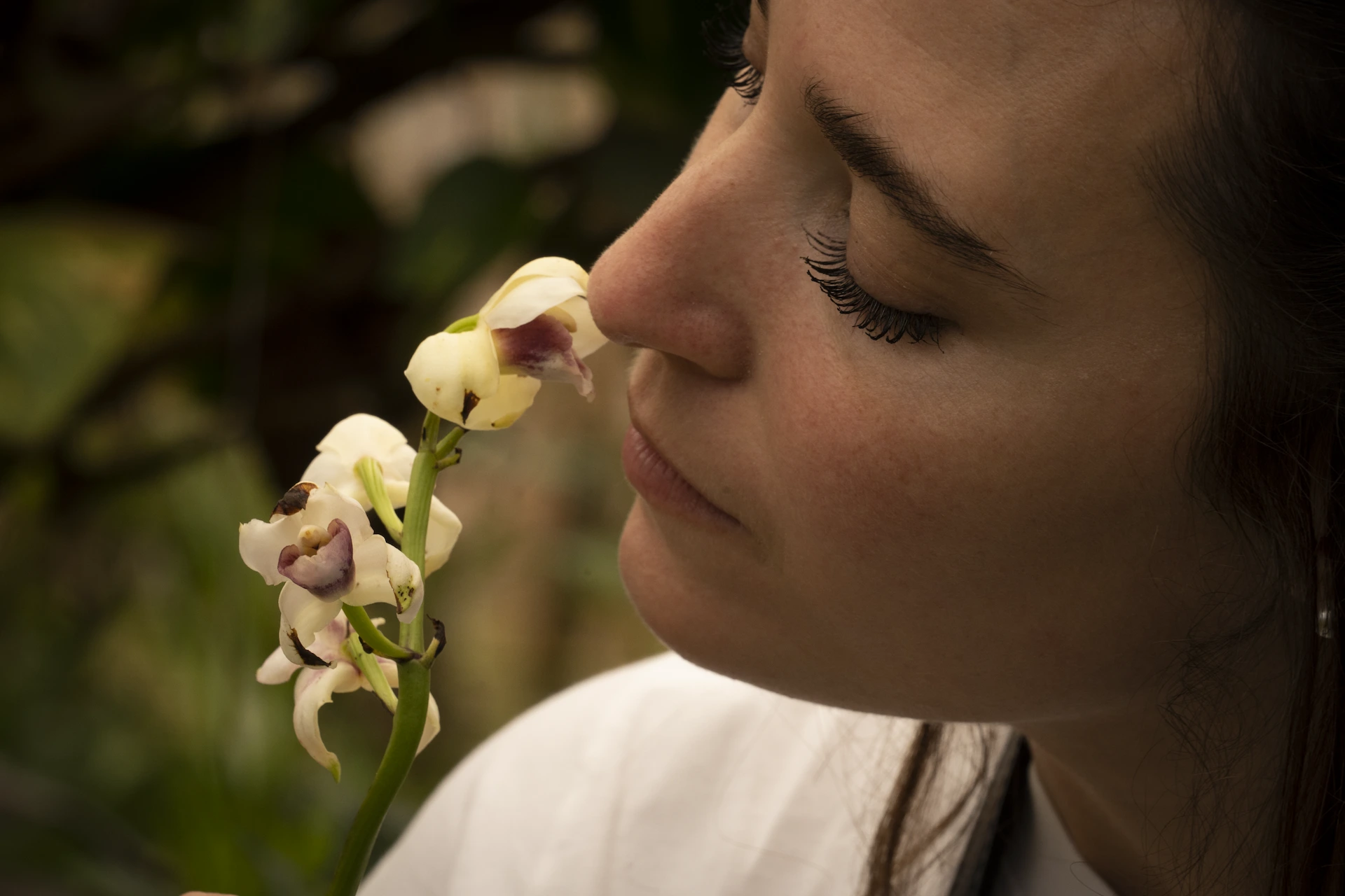 Close-up of a woman smelling a delicate white flower, her face softly lit.