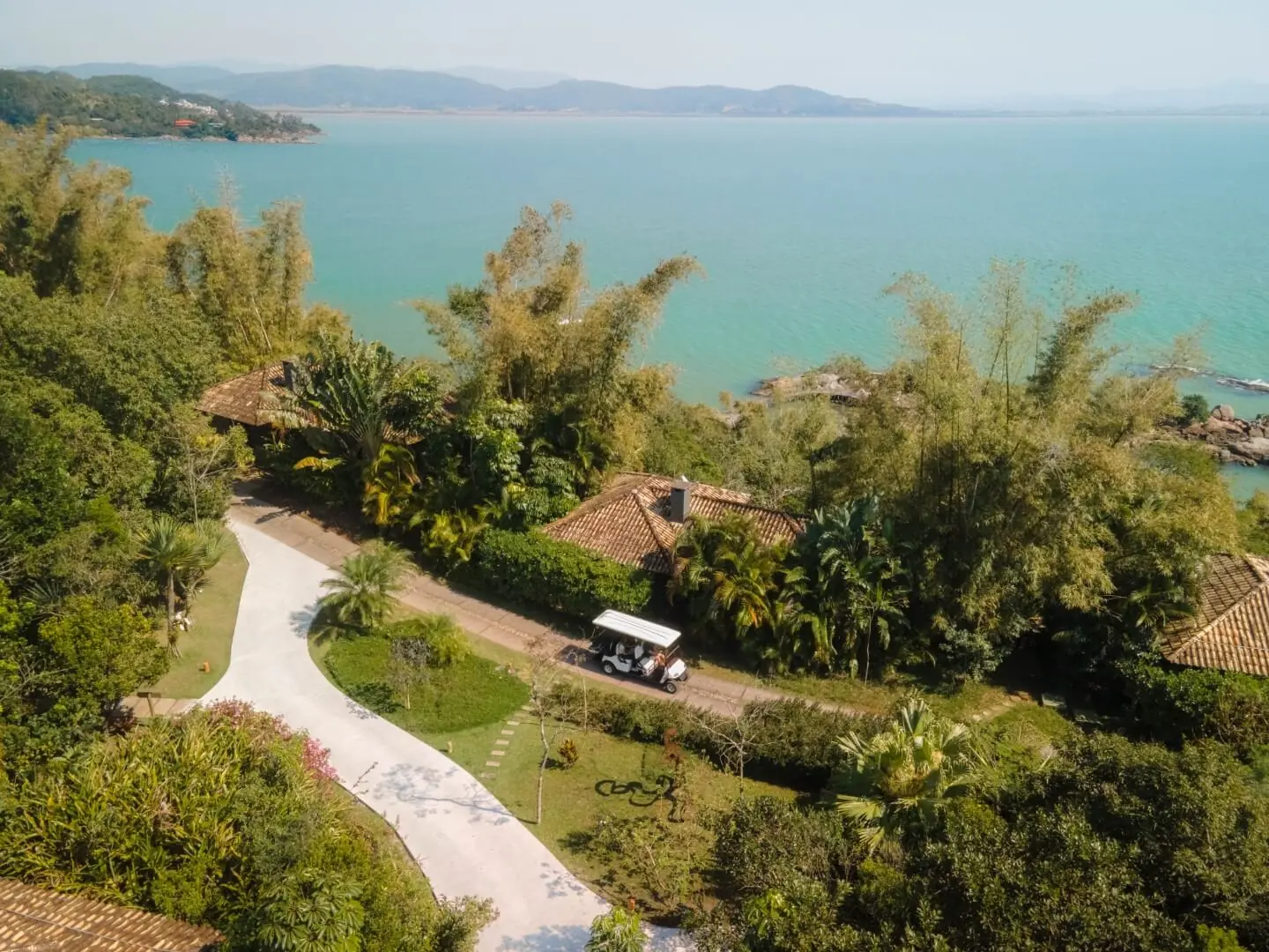 Aerial view of a coastal resort with lush gardens, villas, winding paths, and turquoise ocean beyond.