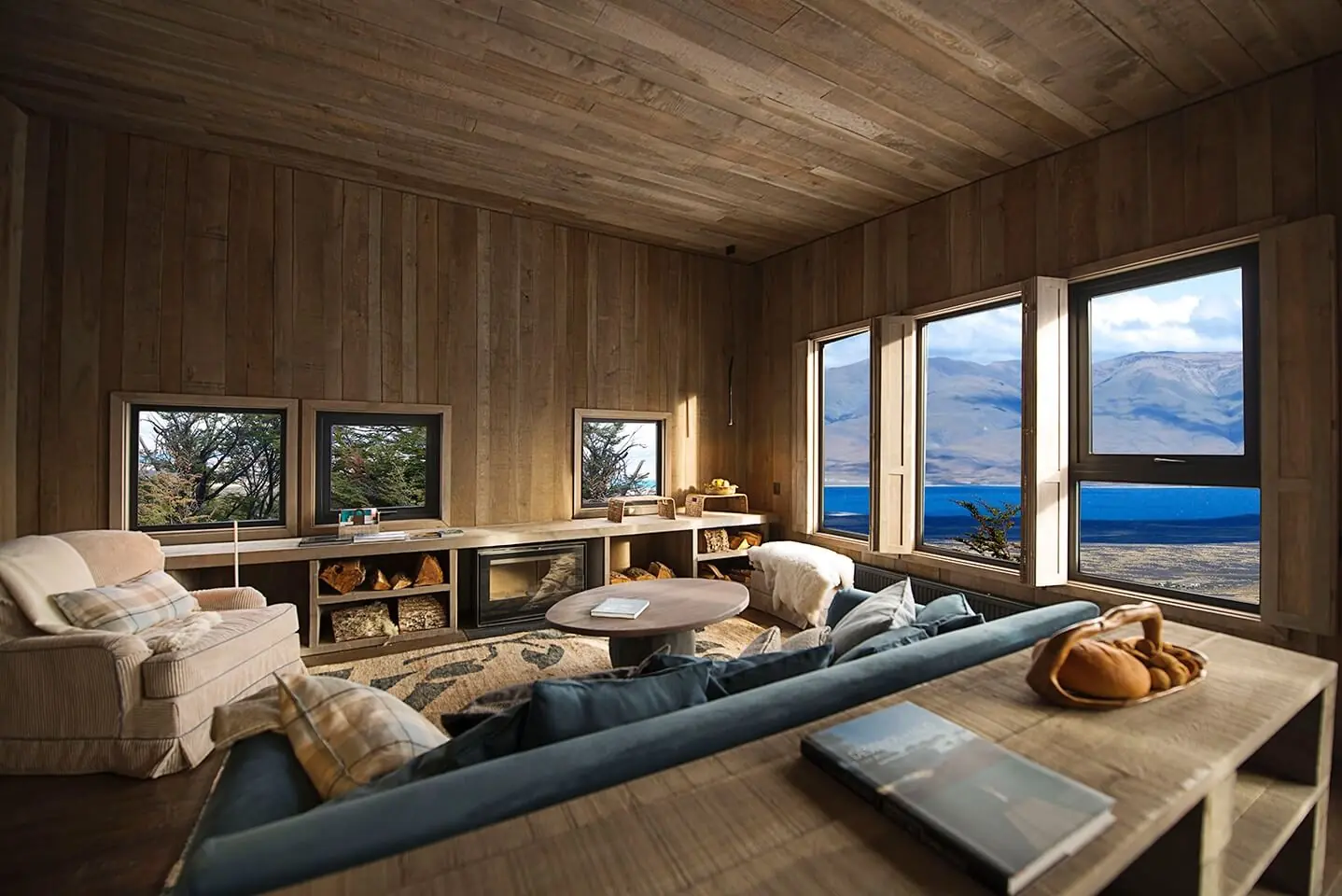 Warm wood-paneled living room with panoramic mountain and lake views, cozy seating, and natural light.