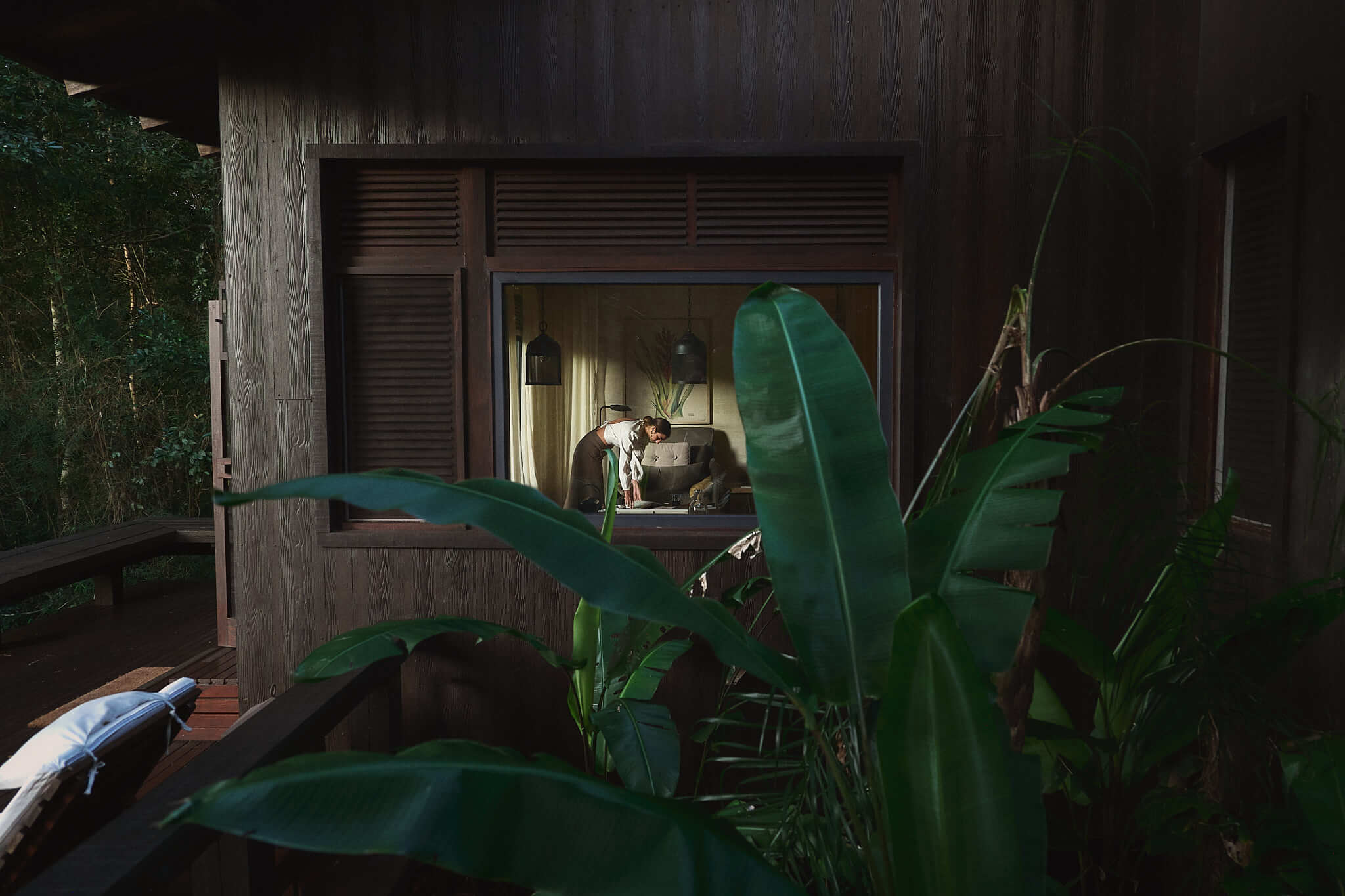 A quiet moment inside a secluded forest cabin, framed by lush greenery and warm interior light.
