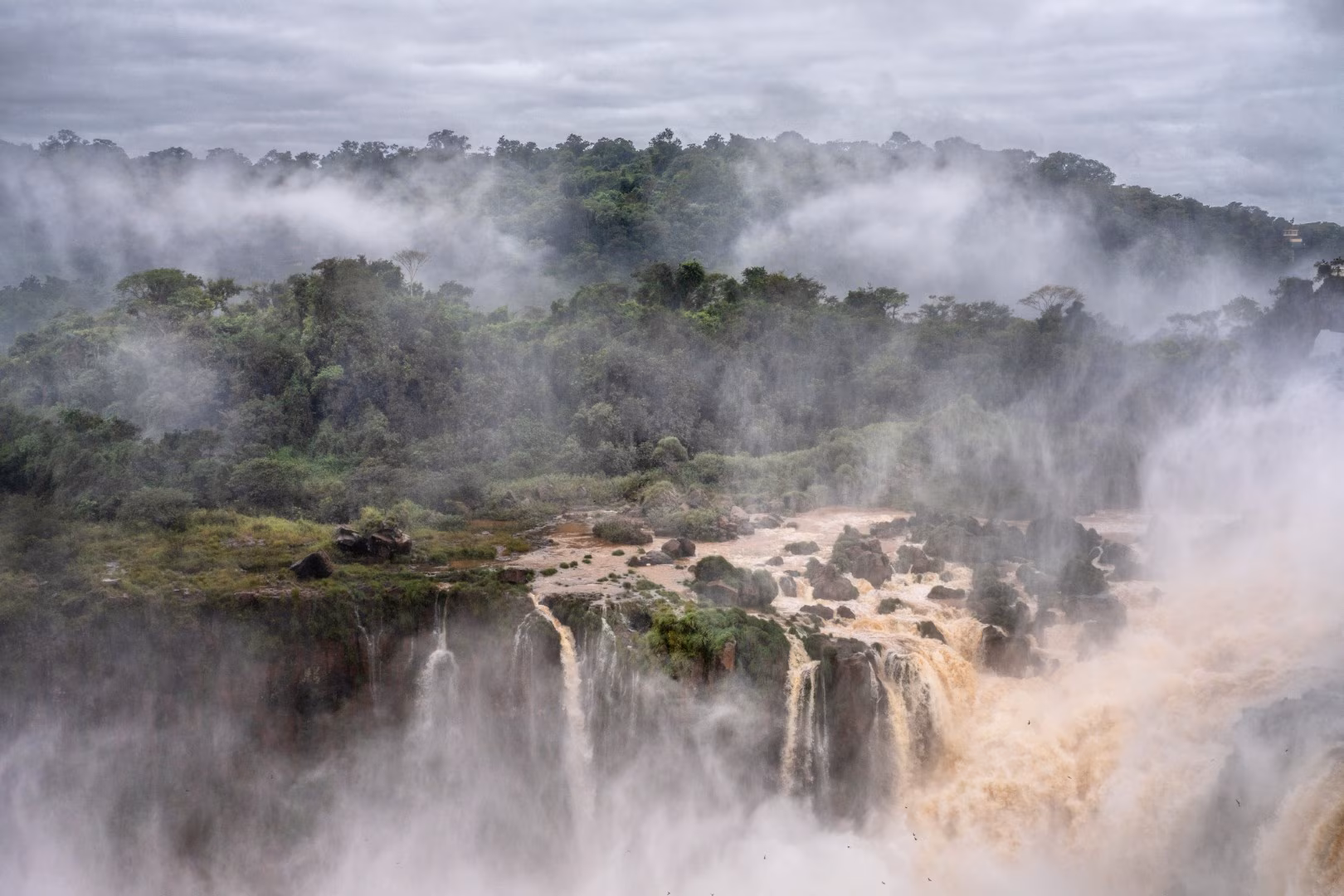 Misty waterfalls cascading through dense rainforest, with powerful flows plunging into a fog-filled gorge.