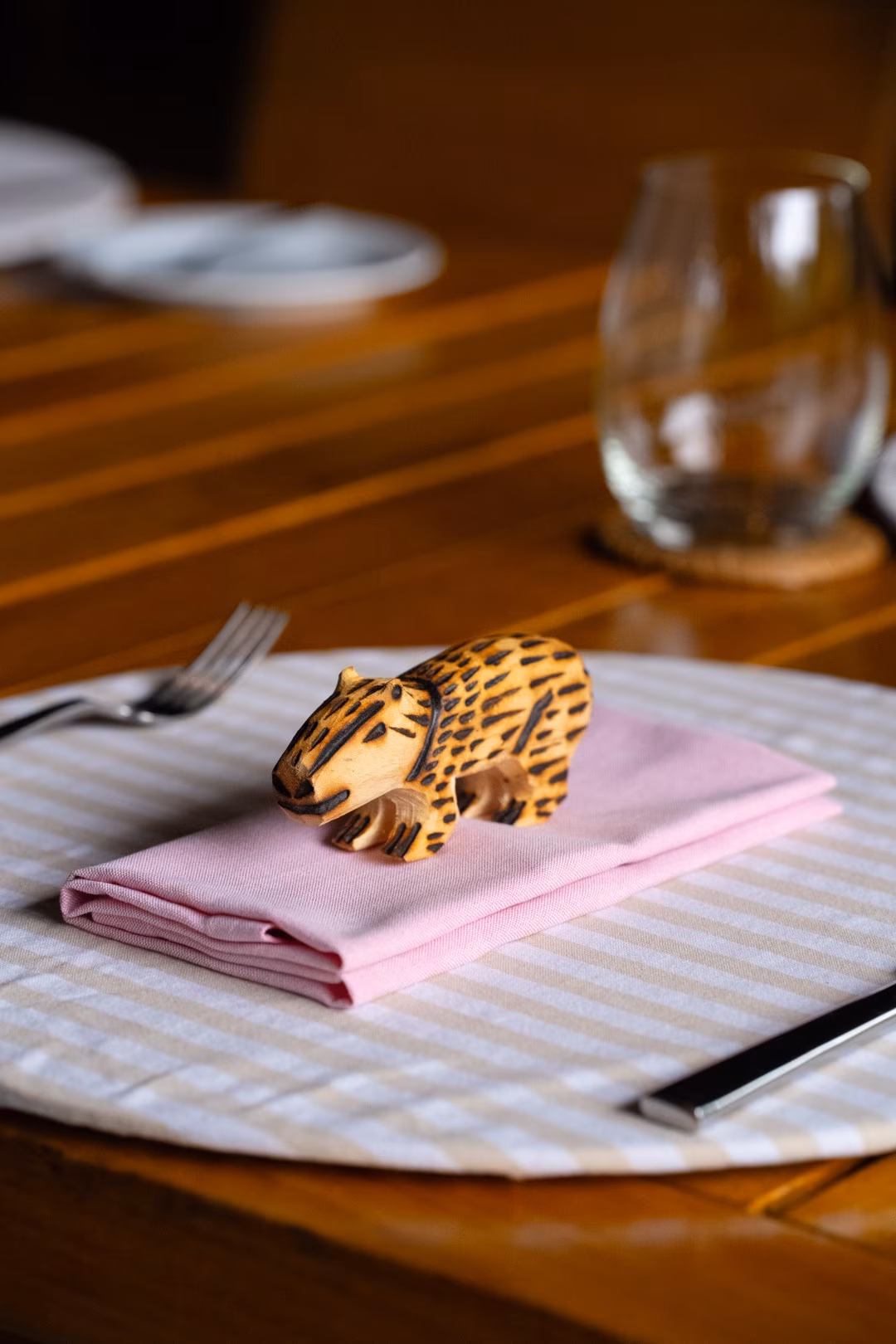 Small carved wooden jaguar placed on a folded pink napkin at a neatly set dining table.