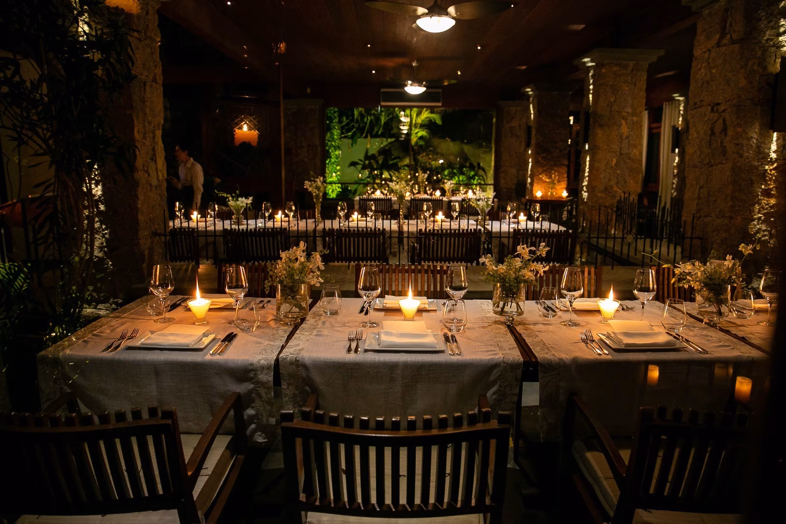 Elegant candlelit dining room with long tables, white linens, floral centerpieces, and warm ambient lighting at night.