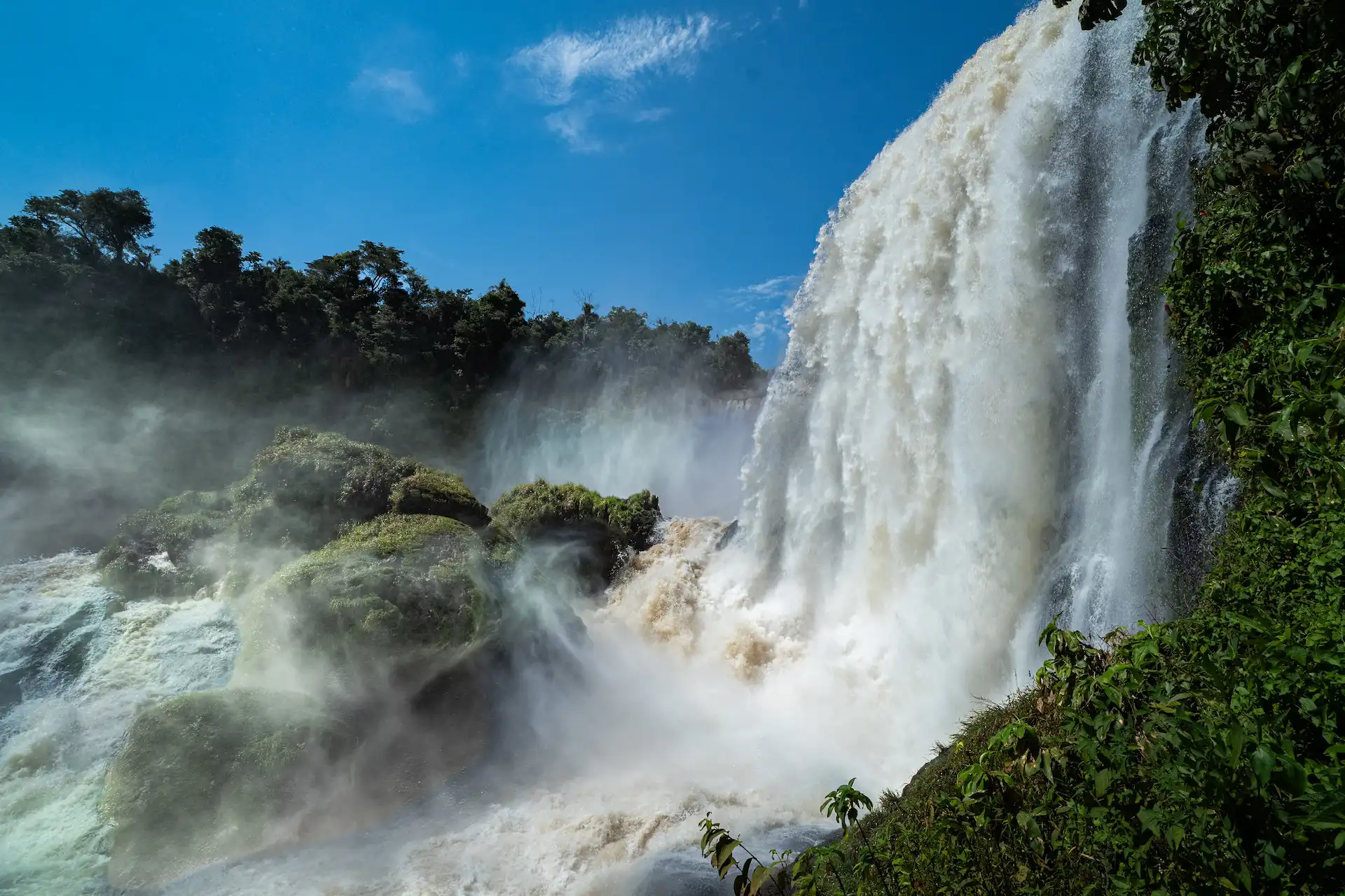 Iguazú Falls cascading through lush subtropical rainforest under blue sky