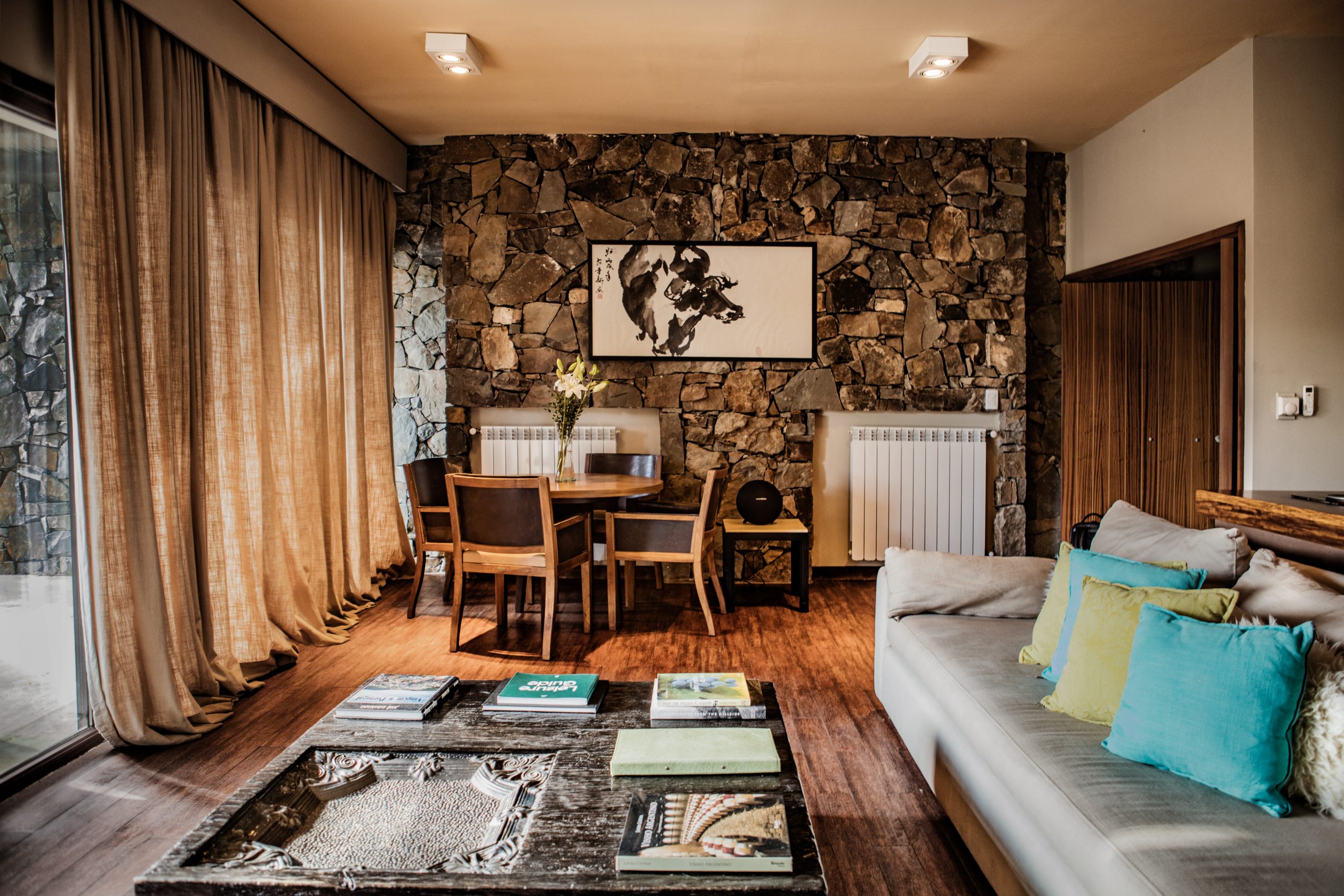 Cozy living room with stone accent wall, wooden dining table, sofa with pillows, and natural light.