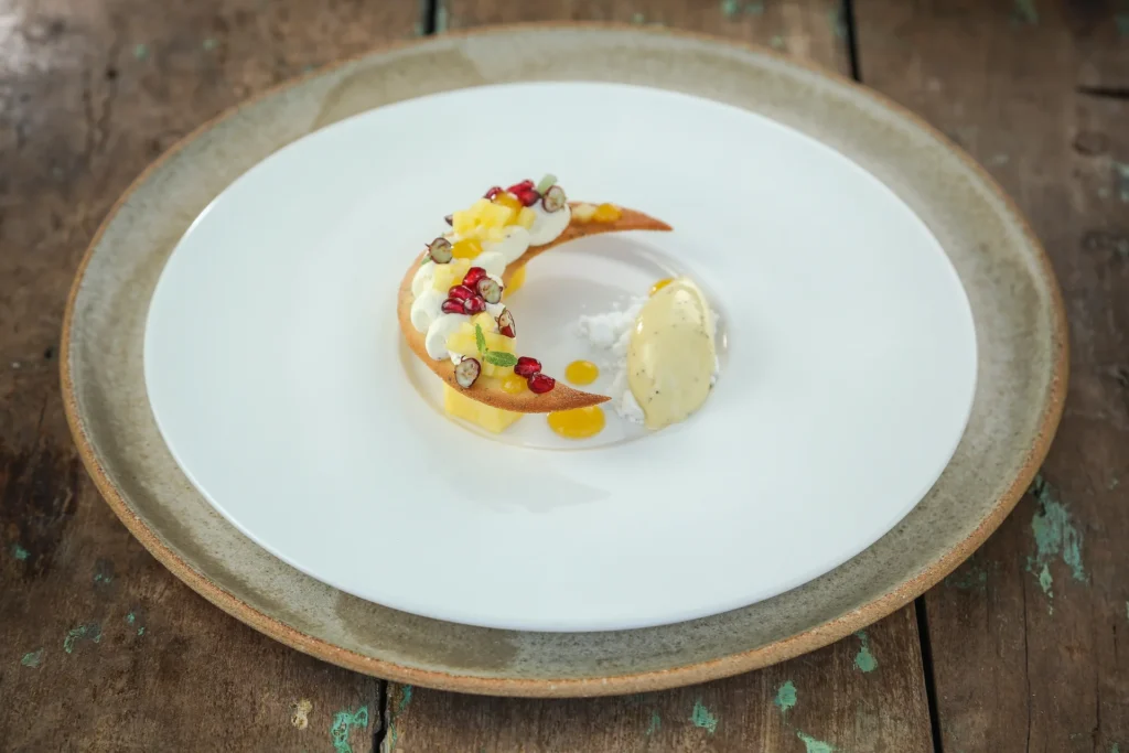 Artfully plated dessert with a crescent pastry, cream, fruit, and a scoop of ice cream on a white plate.