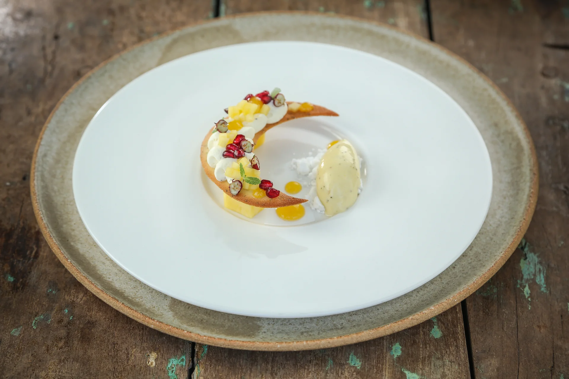 Artfully plated dessert with a crescent pastry, cream, fruit, and a scoop of ice cream on a white plate.