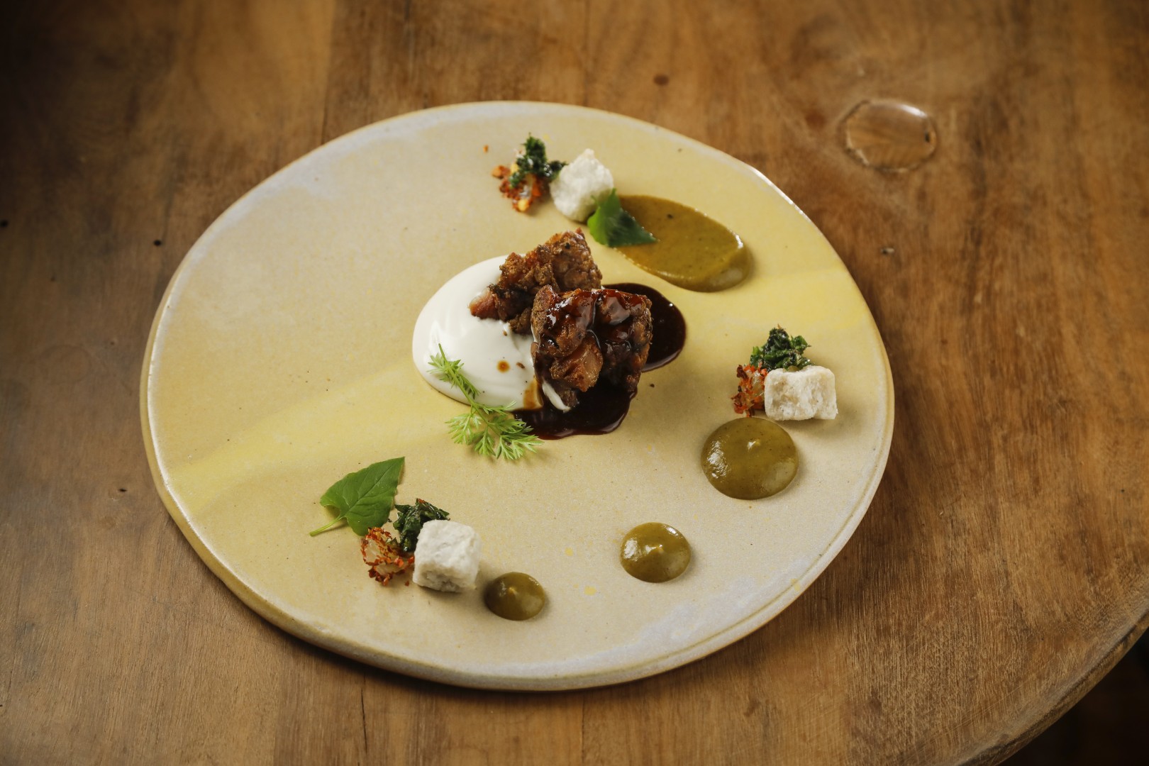 Artfully plated gourmet dish with braised meat, creamy sauce, herb garnishes, and green purées on a ceramic plate.