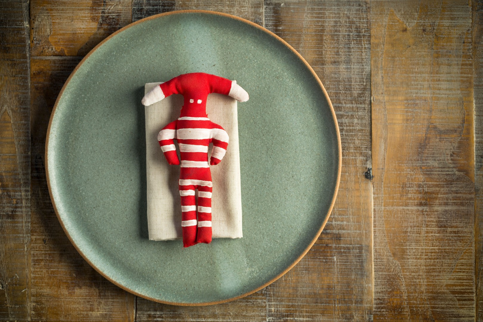 Red and white striped cloth doll shaped like a person, placed on a folded napkin atop a ceramic plate.