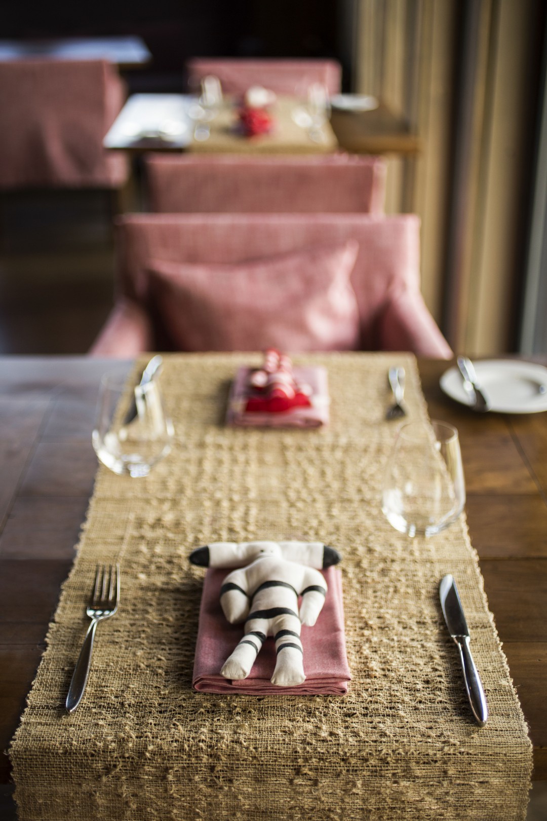 Elegant restaurant table setting with folded napkin centerpiece, placemat, glassware, and soft-focus seating in the background.