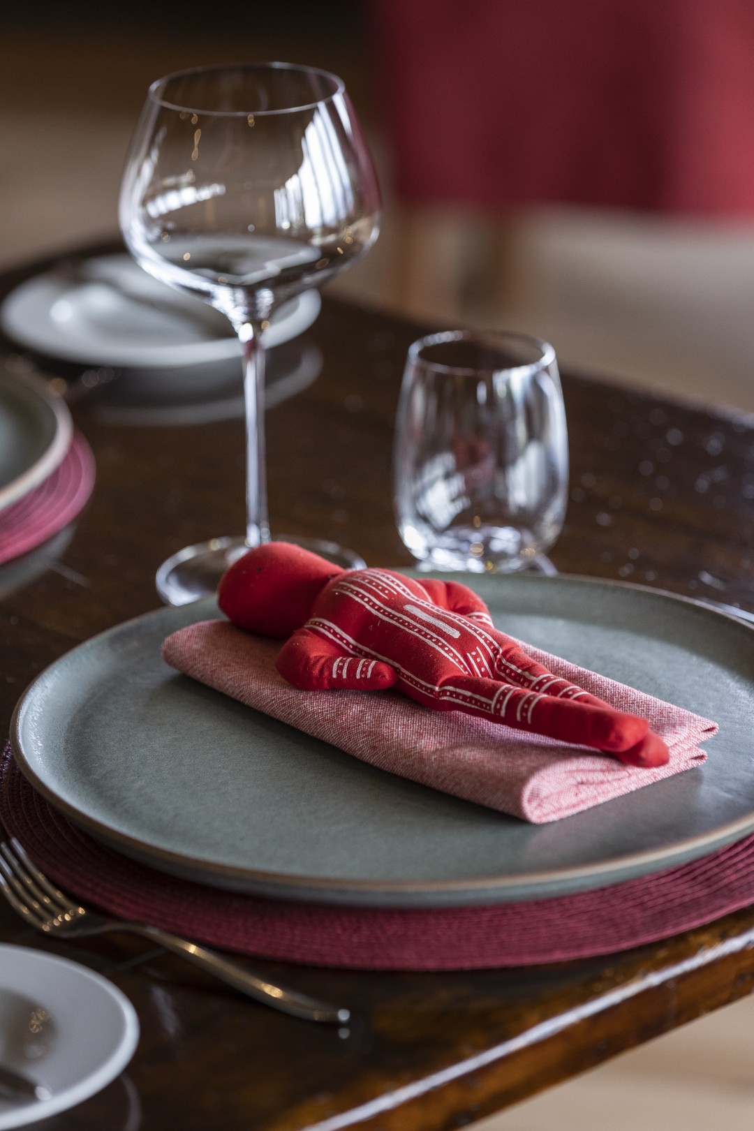 Elegant table setting with stacked plates, red cloth napkin, and wine glasses on a polished wooden table.