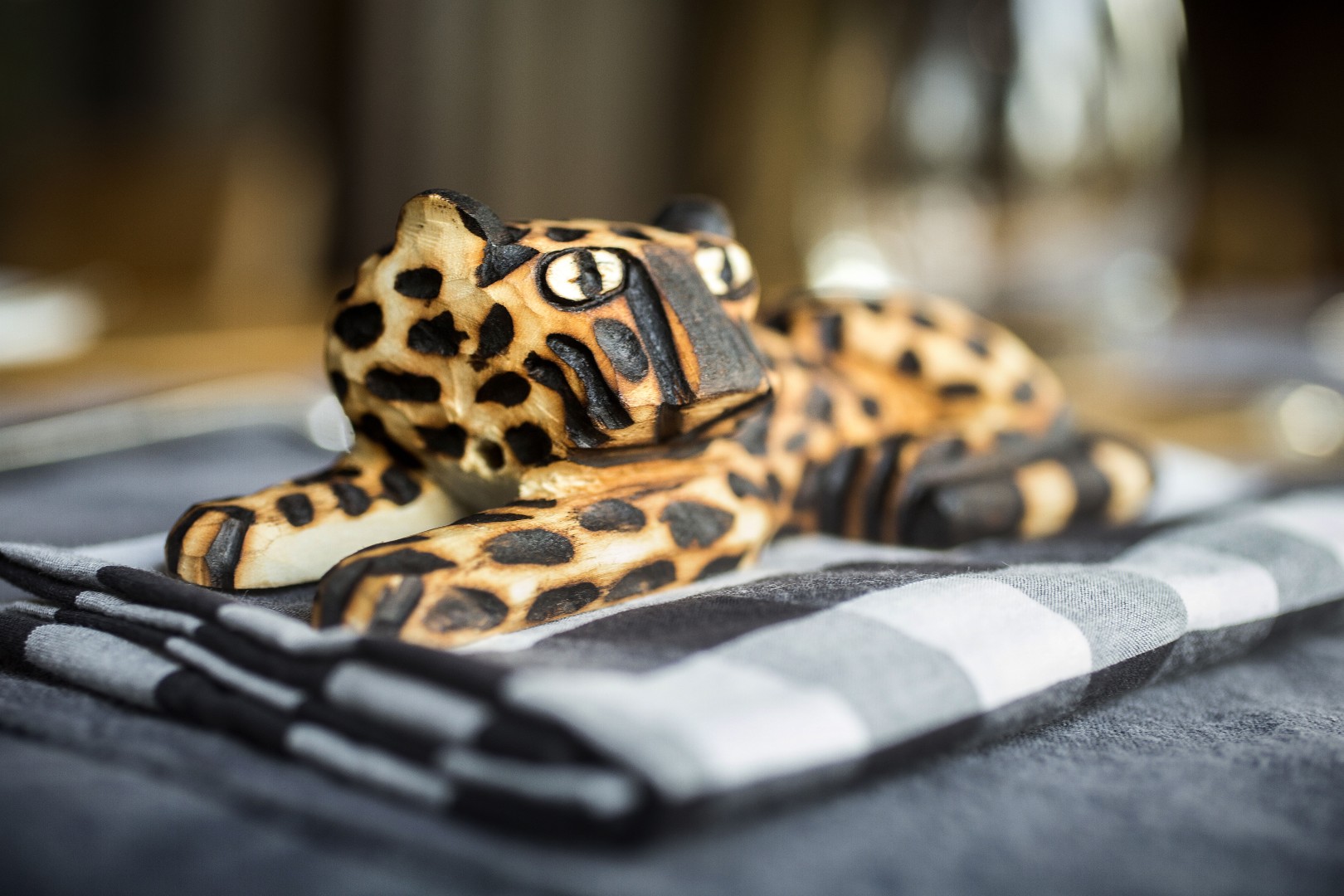 Carved wooden jaguar figurine resting on folded napkin, with spotted details and soft-focus background.