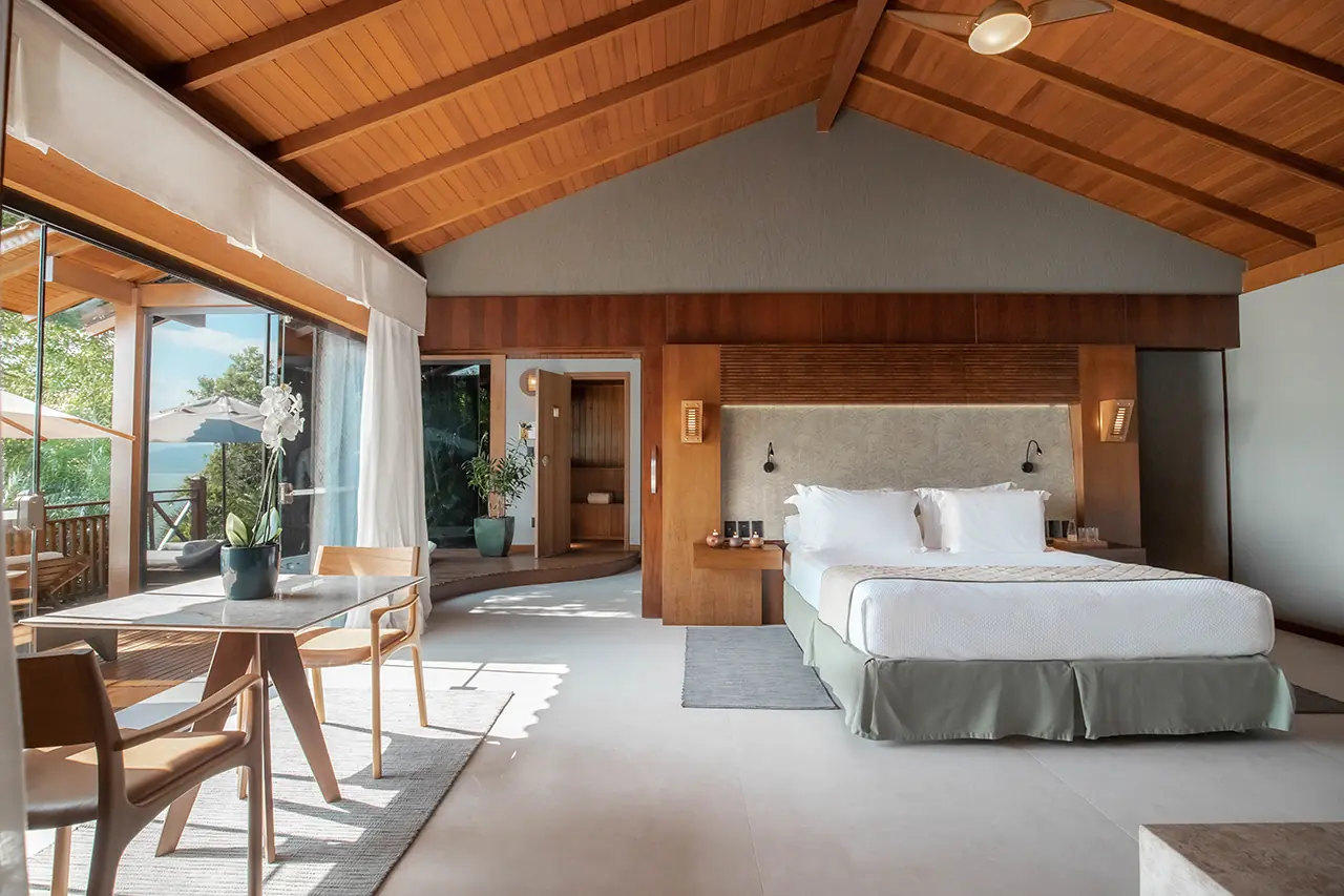 Spacious Luxury Bedroom With Wood Ceiling, King Bed, Seating Area, And Large Windows Opening To A Private Terrace.