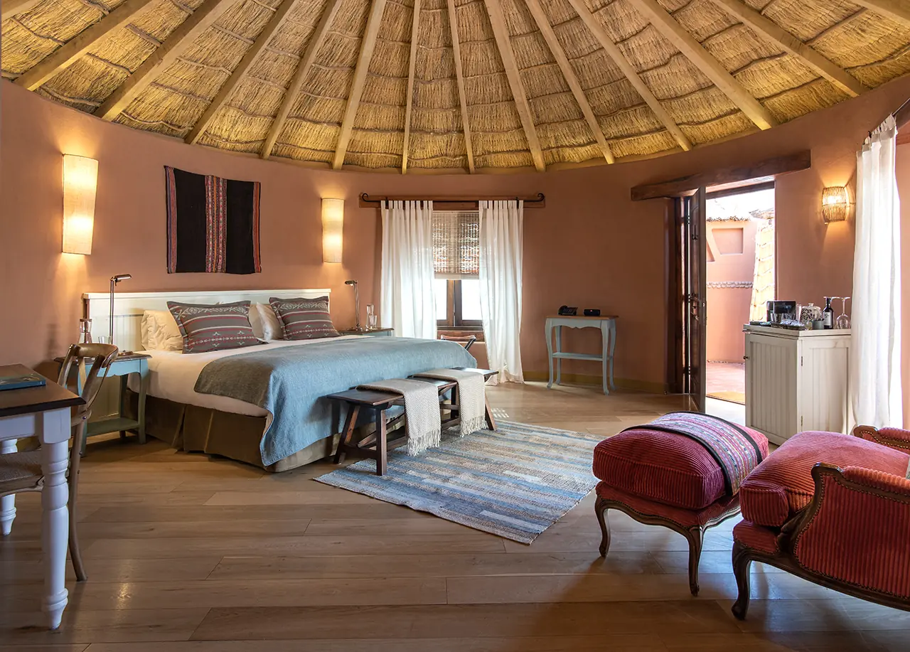 Spacious Rustic Bedroom With A Thatched Ceiling, Large Bed, Warm Lighting, And Cozy Seating Area.