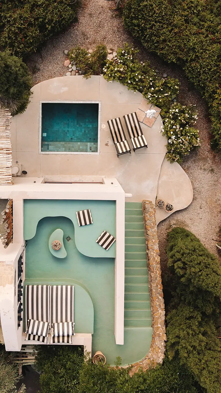 Aerial View Of Modern Pool Terrace With Geometric Pools, Striped Loungers, Stone Steps, And Landscaped Garden Paths.