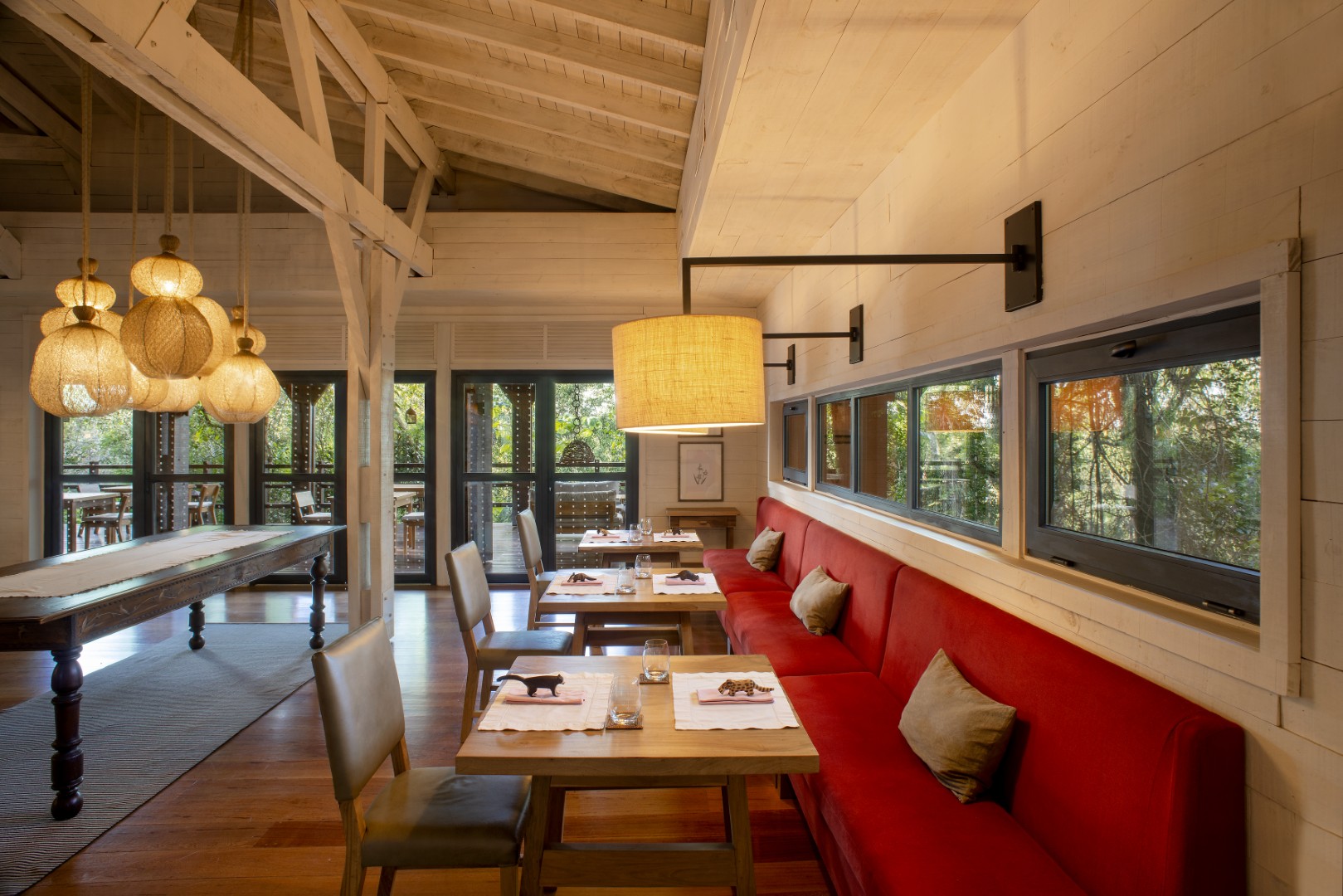 Cozy restaurant dining room with red banquette seating, wooden tables, warm pendant lights, and forest views.