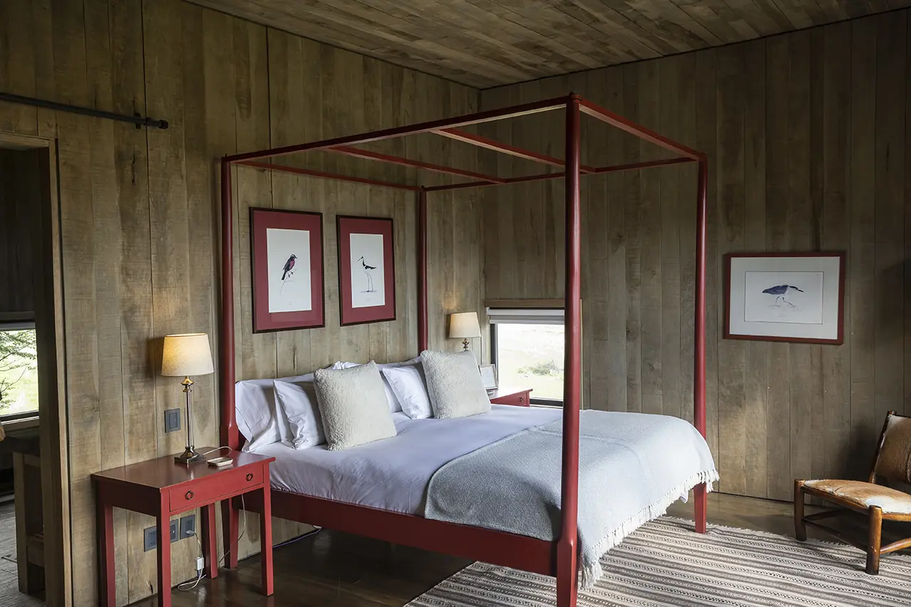 Rustic Bedroom With Red Four-Poster Bed, Wooden Walls, Soft Lighting, And Framed Bird Artwork.