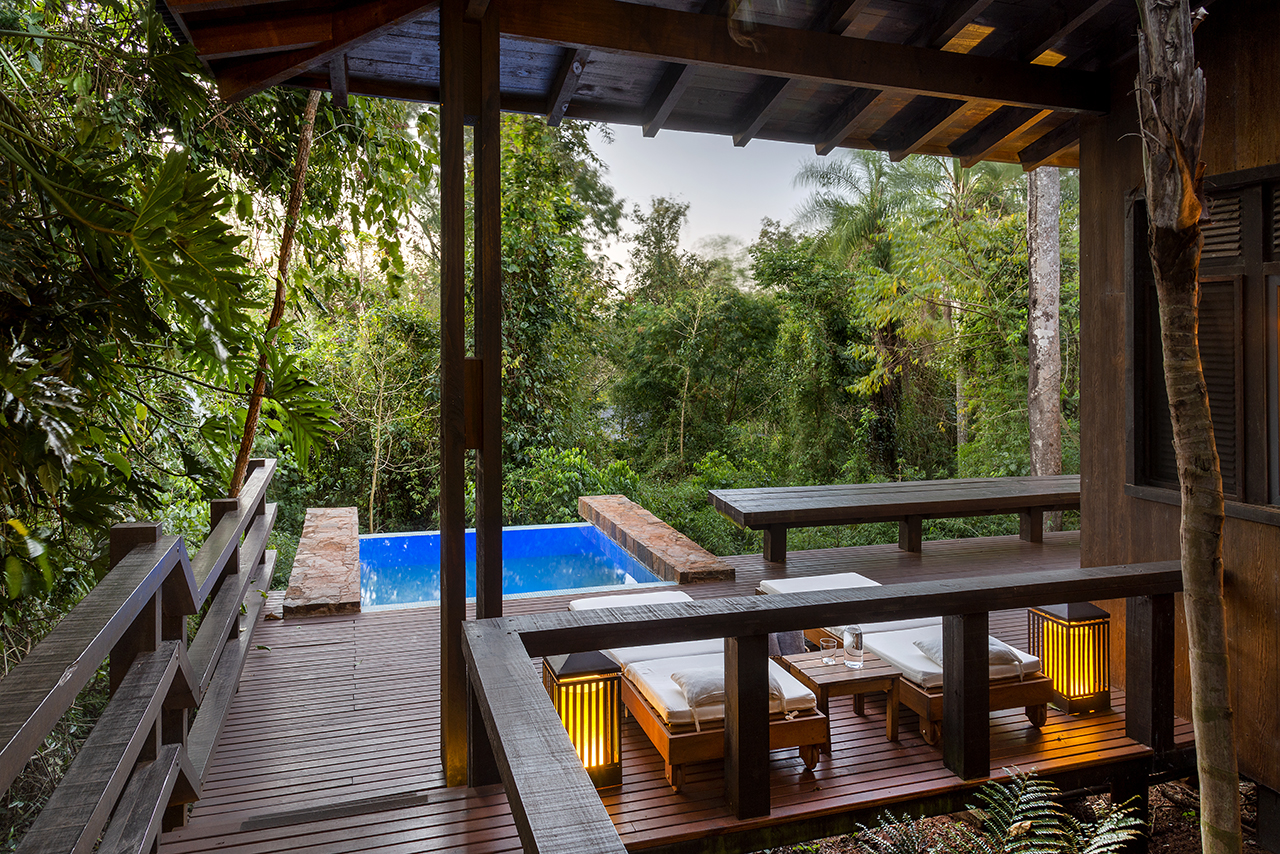 Luxury wooden deck with lounge seating and plunge pool overlooking a lush forest retreat.