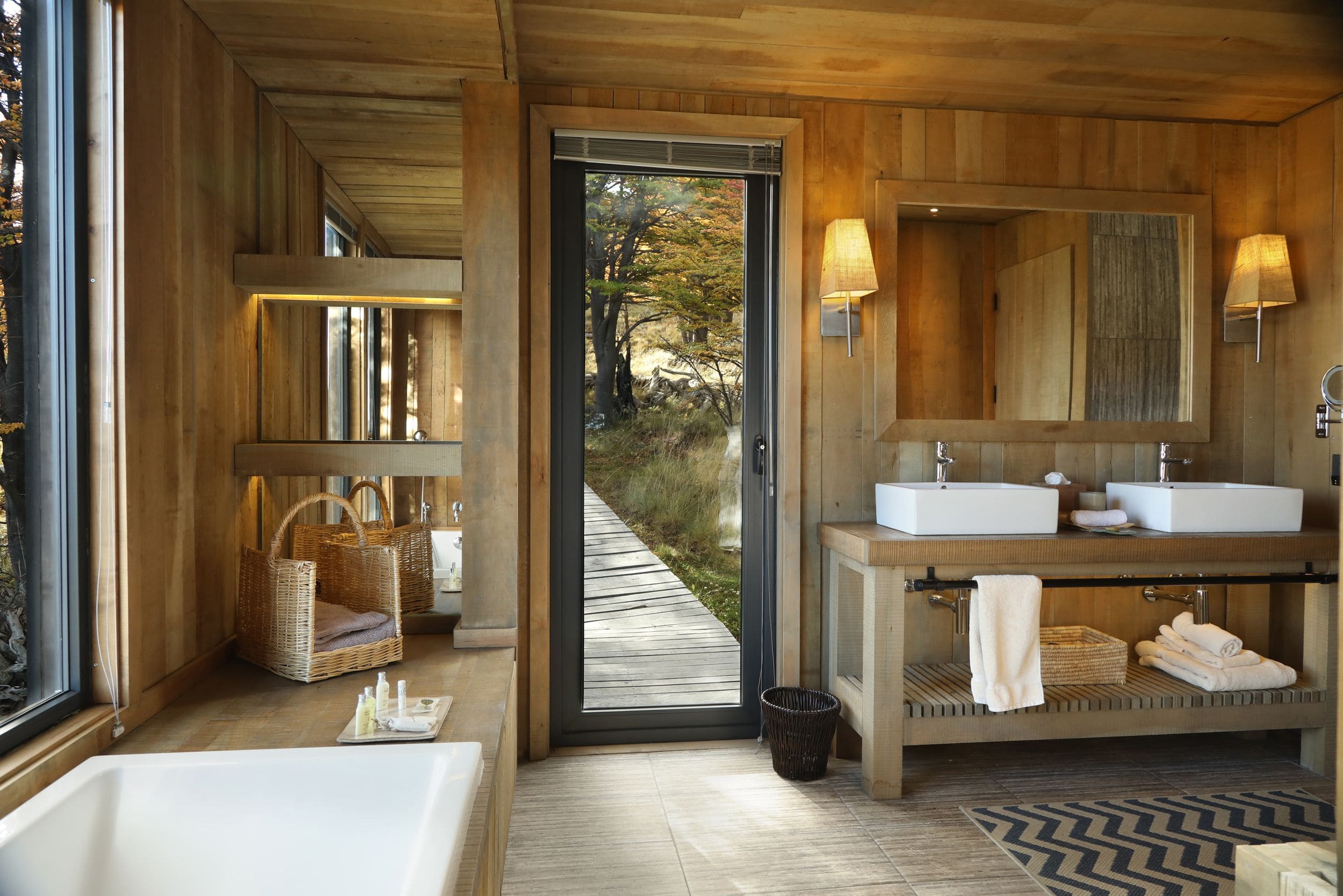 "Luxury bathroom in a private villa at Awasi Patagonia in Torres del Paine National Park, Chile, featuring a deep soaking bathtub, separate shower, double sinks, and a large mirror. The villa is crafted from native wood with decor inspired by Patagonian shelters, offering privacy and views of the forest, lake, and surrounding national park.