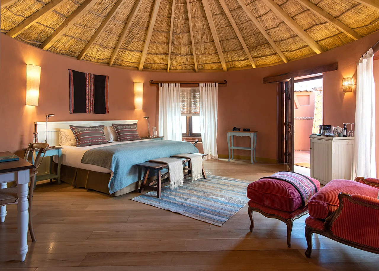 Spacious rustic bedroom with a thatched ceiling, large bed, warm lighting, and cozy seating area.