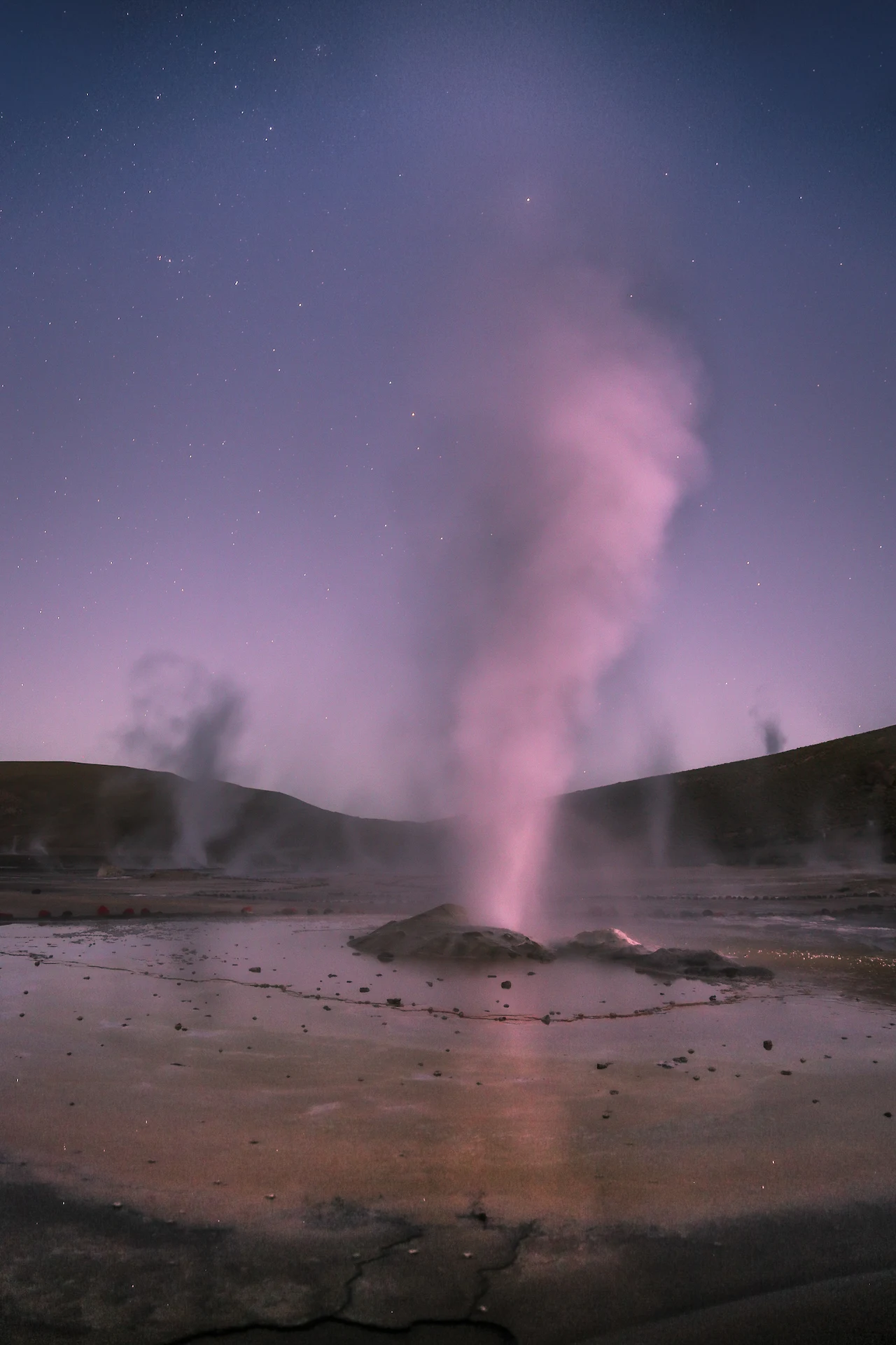 Steam rising from El Tatio Geysers at dawn under a starry sky in the Atacama Desert
