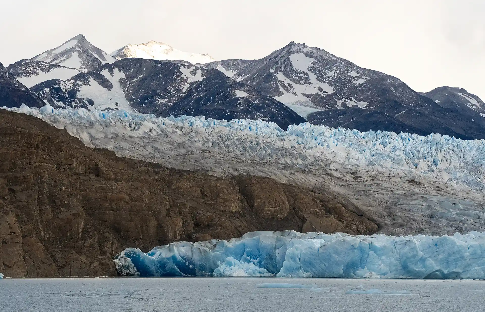 Massive blue glacier meeting the water at the base of rugged, snow-peaked mountains in Patagonia