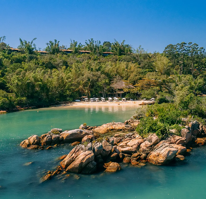 Aerial view of a secluded tropical bay with turquoise water, rocky shore, and villas nestled in a lush green forest