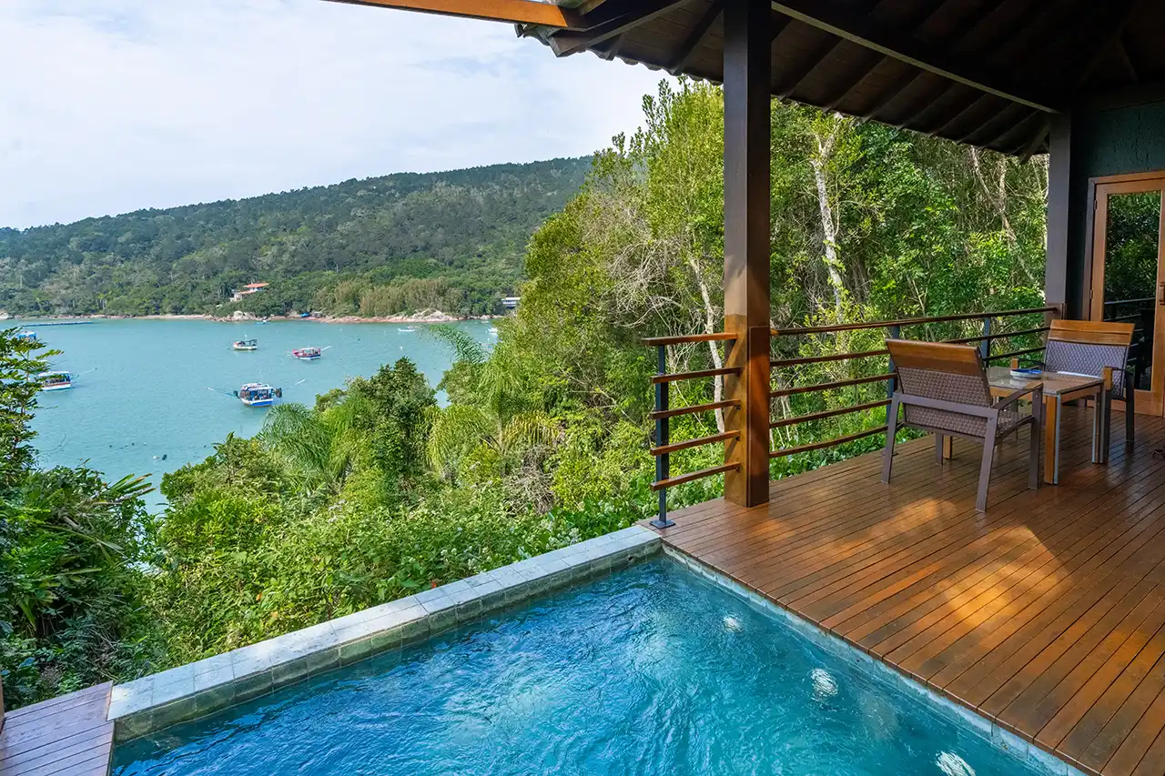 Deck with a small pool overlooking a turquoise bay and surrounding forest.
