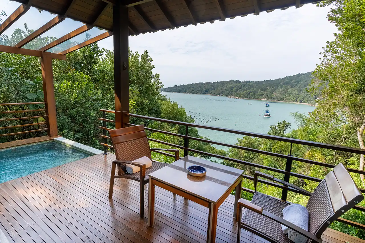 Deck with wicker chairs and a small pool overlooking a forested bay.