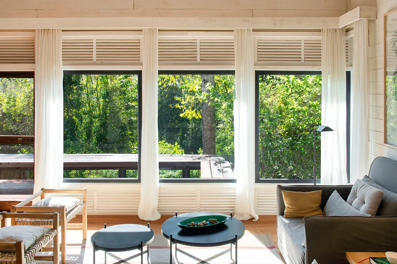 Living room with large windows, gray sofa, and forest views.