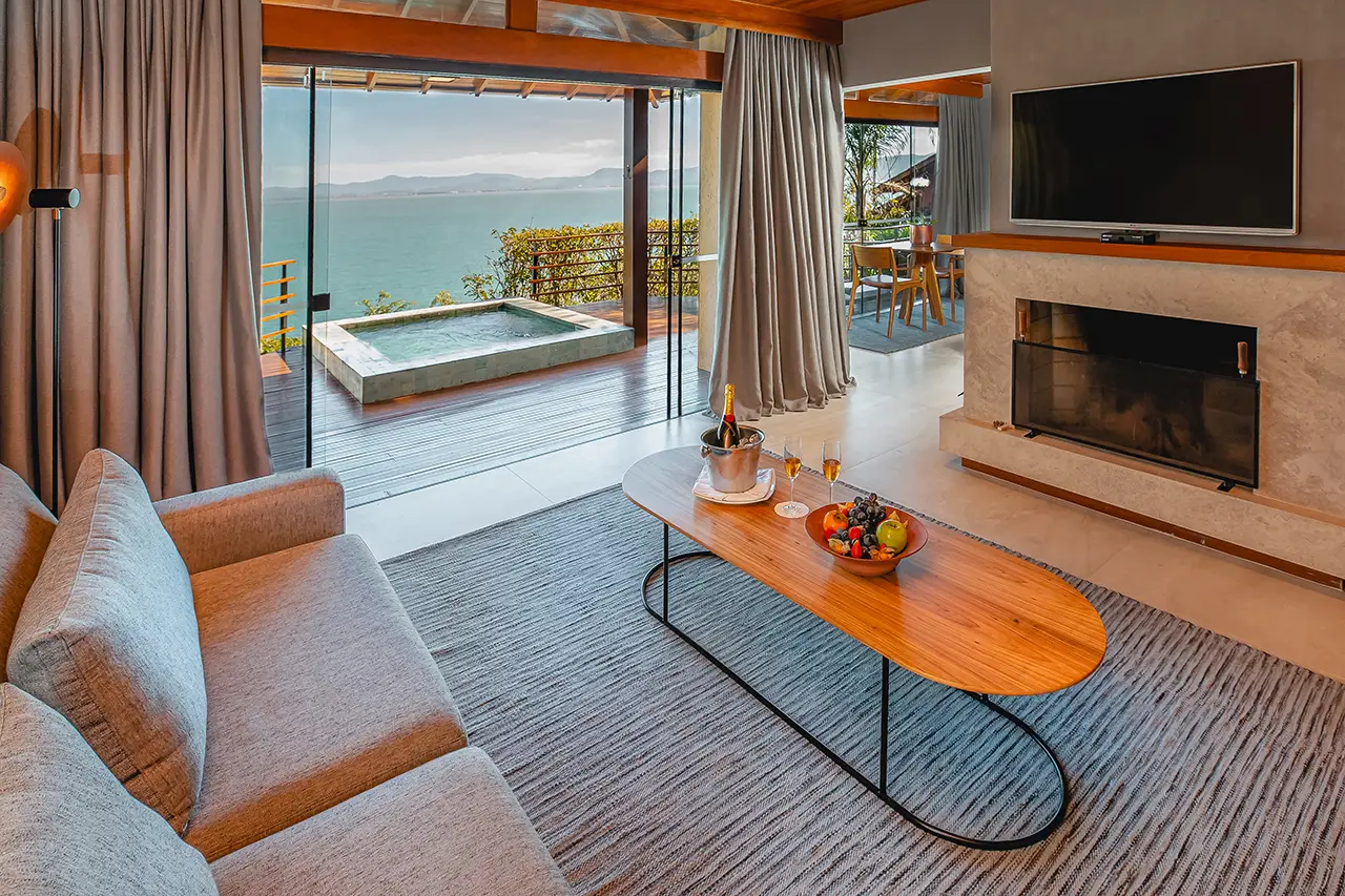 Living room with ocean view, gray sofa, fireplace, and deck with a small hot tub.