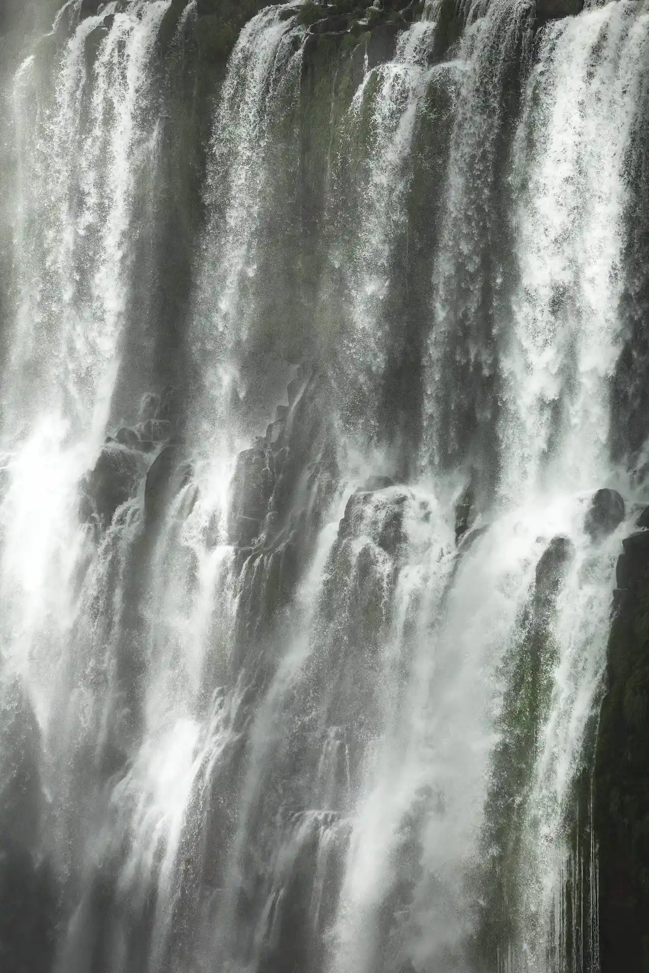 Tall waterfall cascading down dark rocks with mist and white froth.