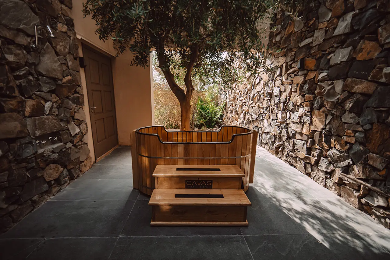 Wooden soaking tub between stone walls with stairs and a tree behind it, marked with “CAVAS Wine Lodge.”