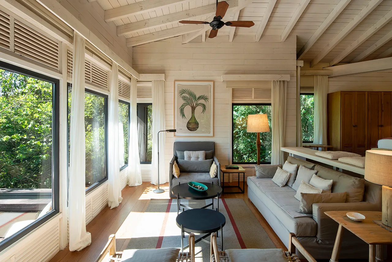 Bright rustic living room with exposed beams, large windows, gray seating, and a cozy, nature‑inspired décor.