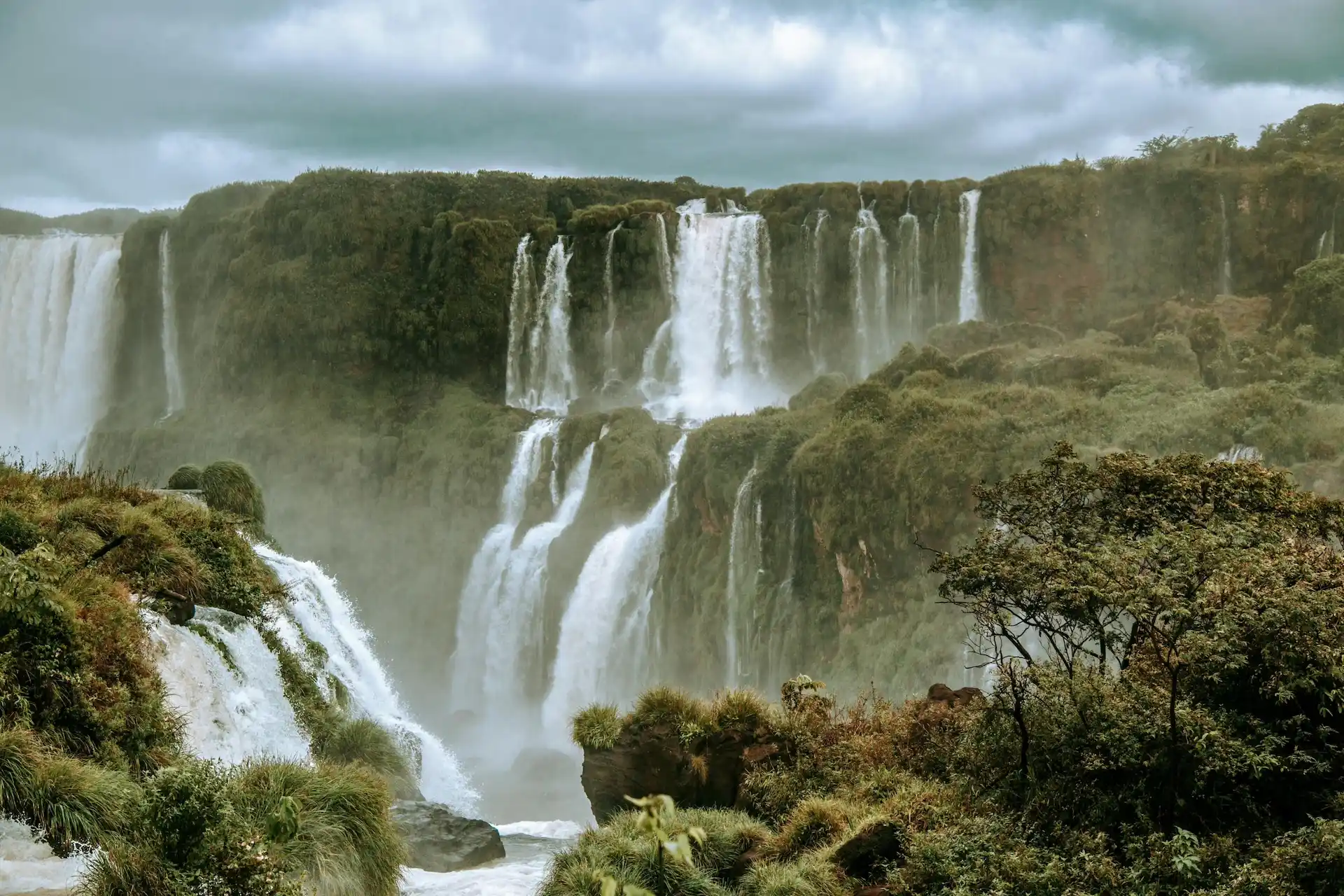 Powerful waterfalls cascading over lush cliffs surrounded by mist and dense green forest.