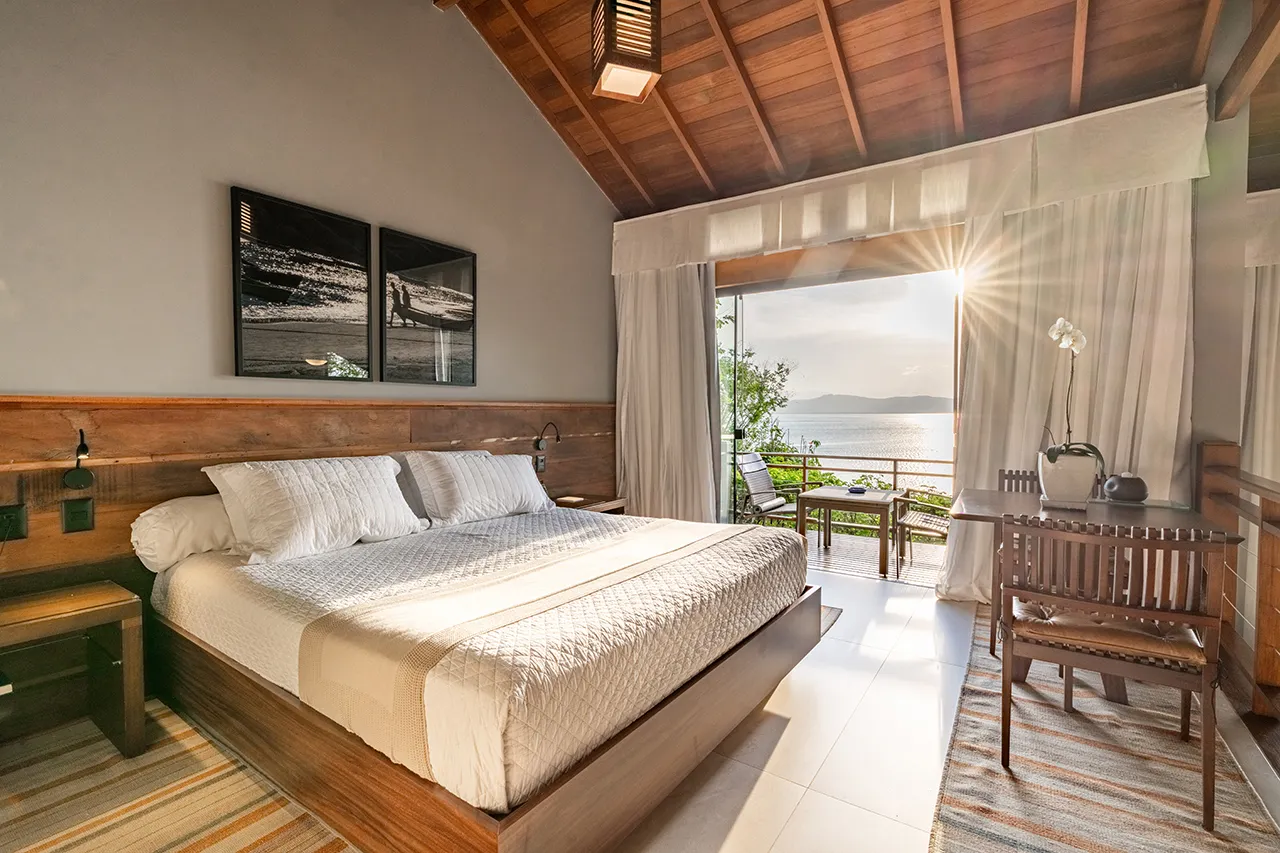 Bright, rustic‑elegant bedroom with lake‑view terrace, wooden beams, and soft morning light.