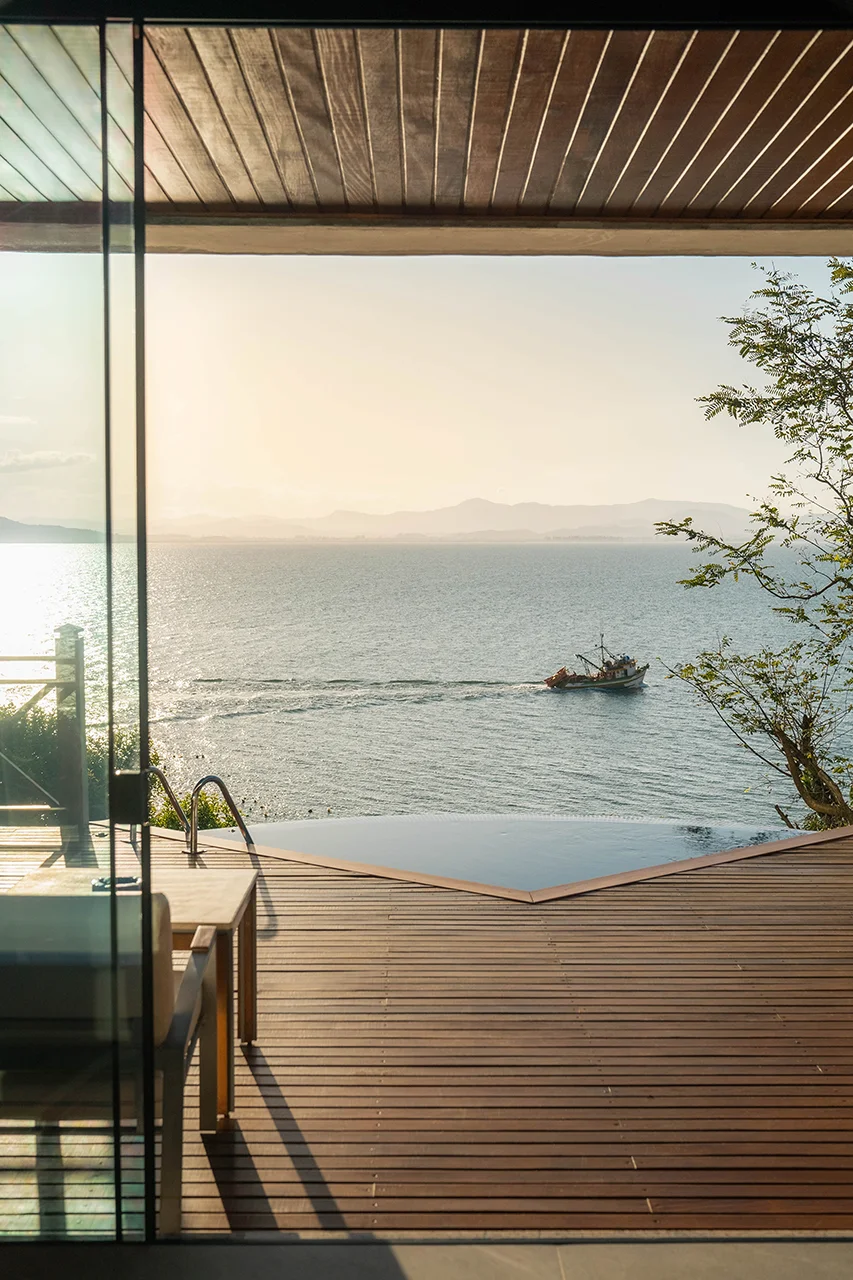 Wooden terrace with an infinity pool overlooking the sea and a boat in the distance