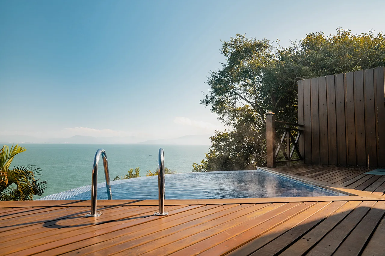Infinity pool with wooden deck overlooking the ocean and surrounding greenery