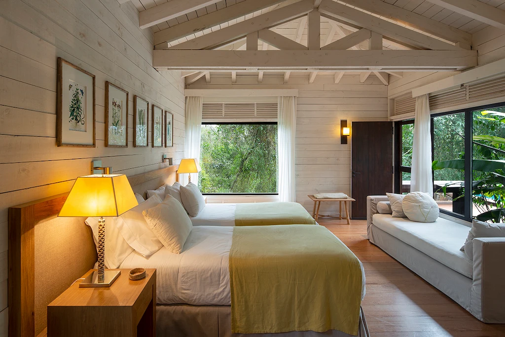 Bright twin bedroom with wooden beams, large windows, and cozy natural decor