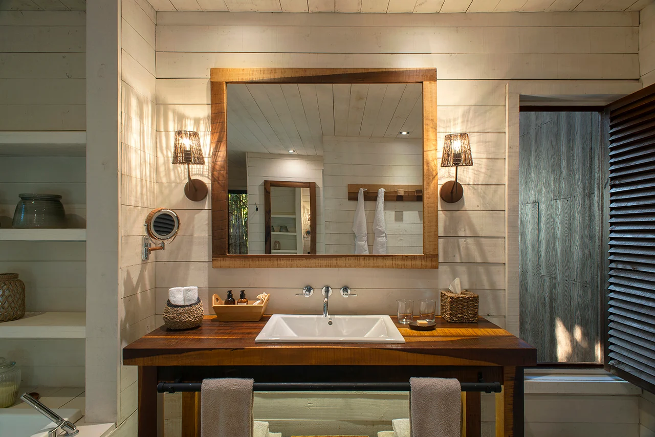Bright wooden bathroom with single sink, large mirror, and warm ambient lighting