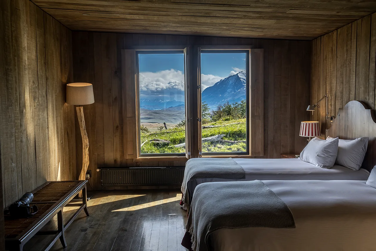 Cozy twin bedroom with wooden interiors and large windows overlooking a mountain landscape