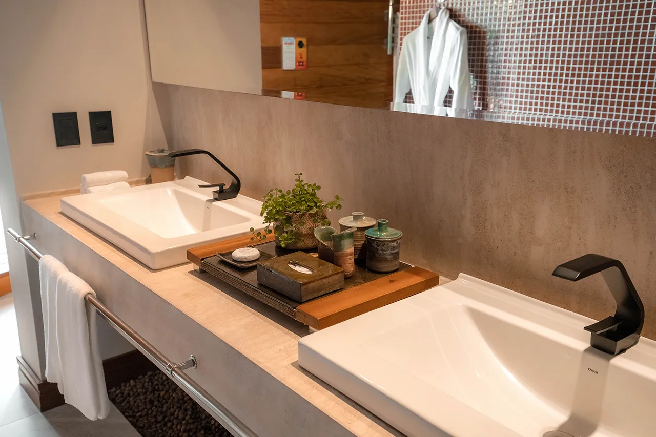 Modern double-sink bathroom vanity with black faucets, neutral stone countertop, and decorative tray with plants and toiletries