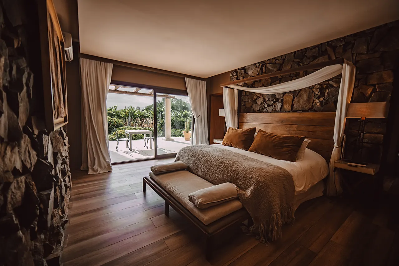 Elegant bedroom with canopy bed stone wall wooden floors and terrace access creating a warm relaxing atmosphere