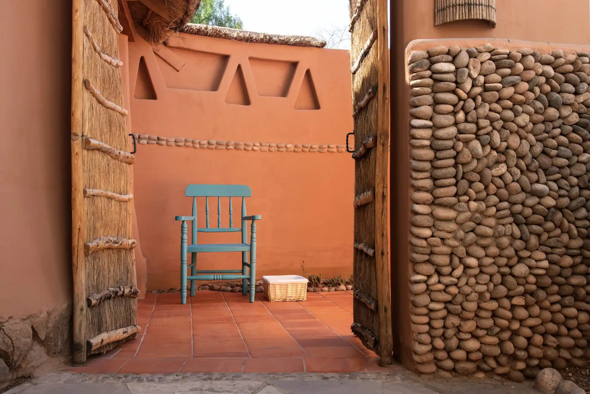 Adobe courtyard entrance with wooden doors stone wall and a blue chair creating a rustic peaceful setting