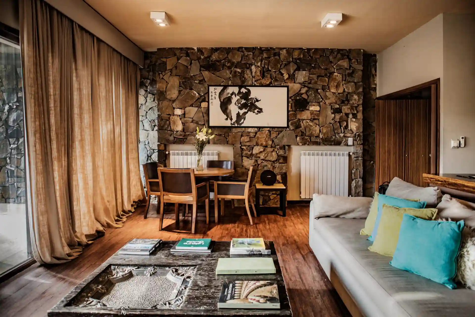 Modern living room with stone wall dining area wooden furniture and large windows with soft natural light