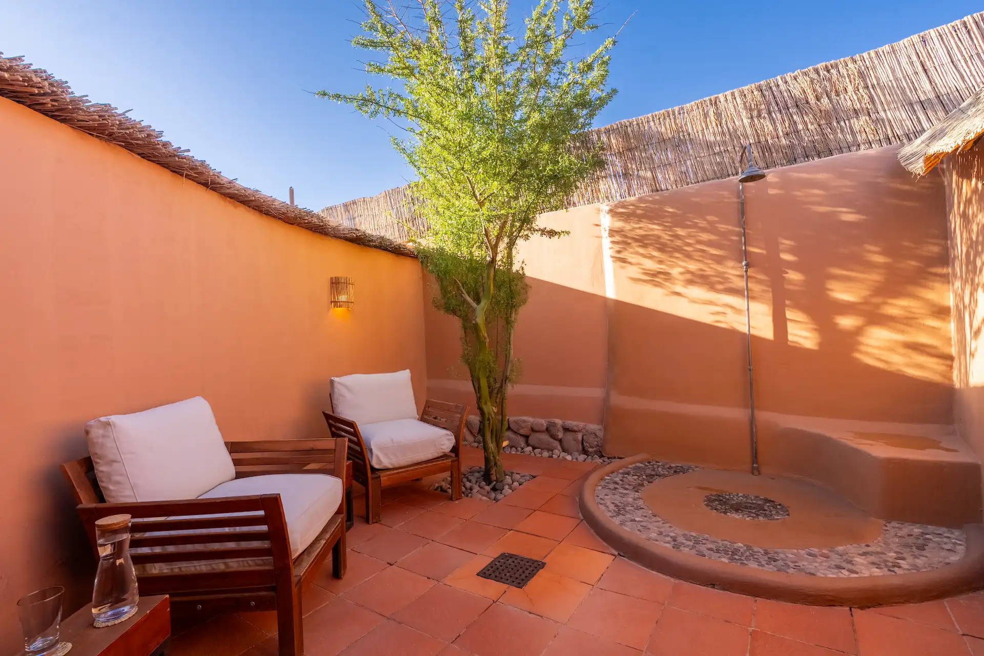 Outdoor shower courtyard with adobe walls seating area and tree under clear blue sky