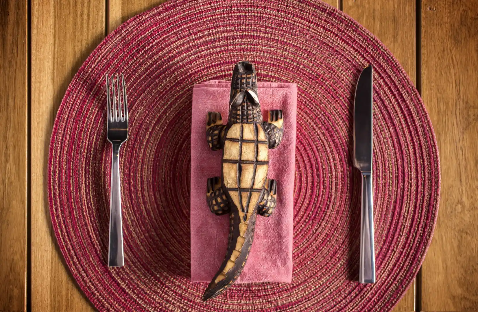 Decorative table setting with woven placemat cutlery and carved wooden lizard on a folded napkin