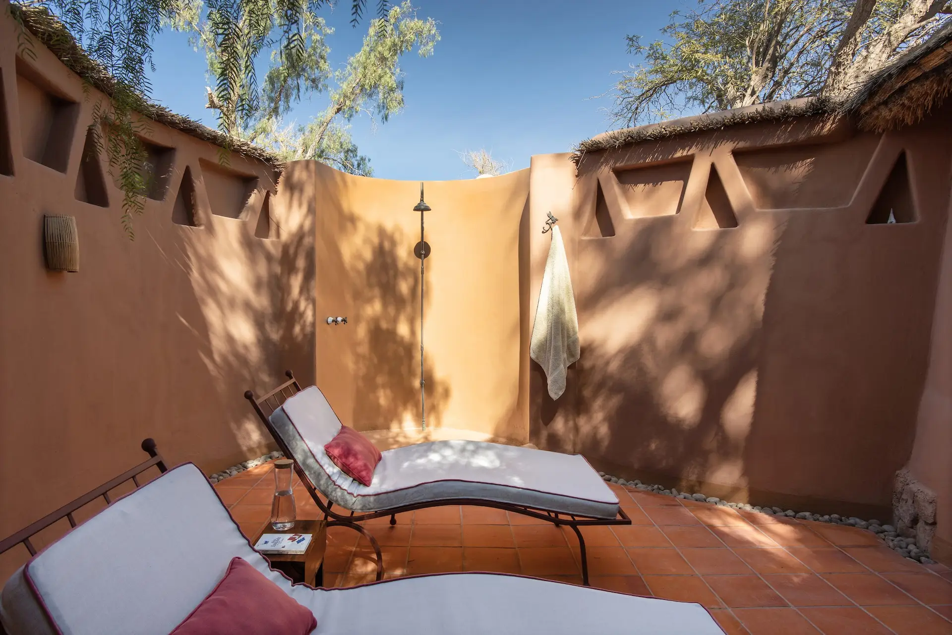 Outdoor shower patio with sun loungers surrounded by adobe walls under clear blue sky