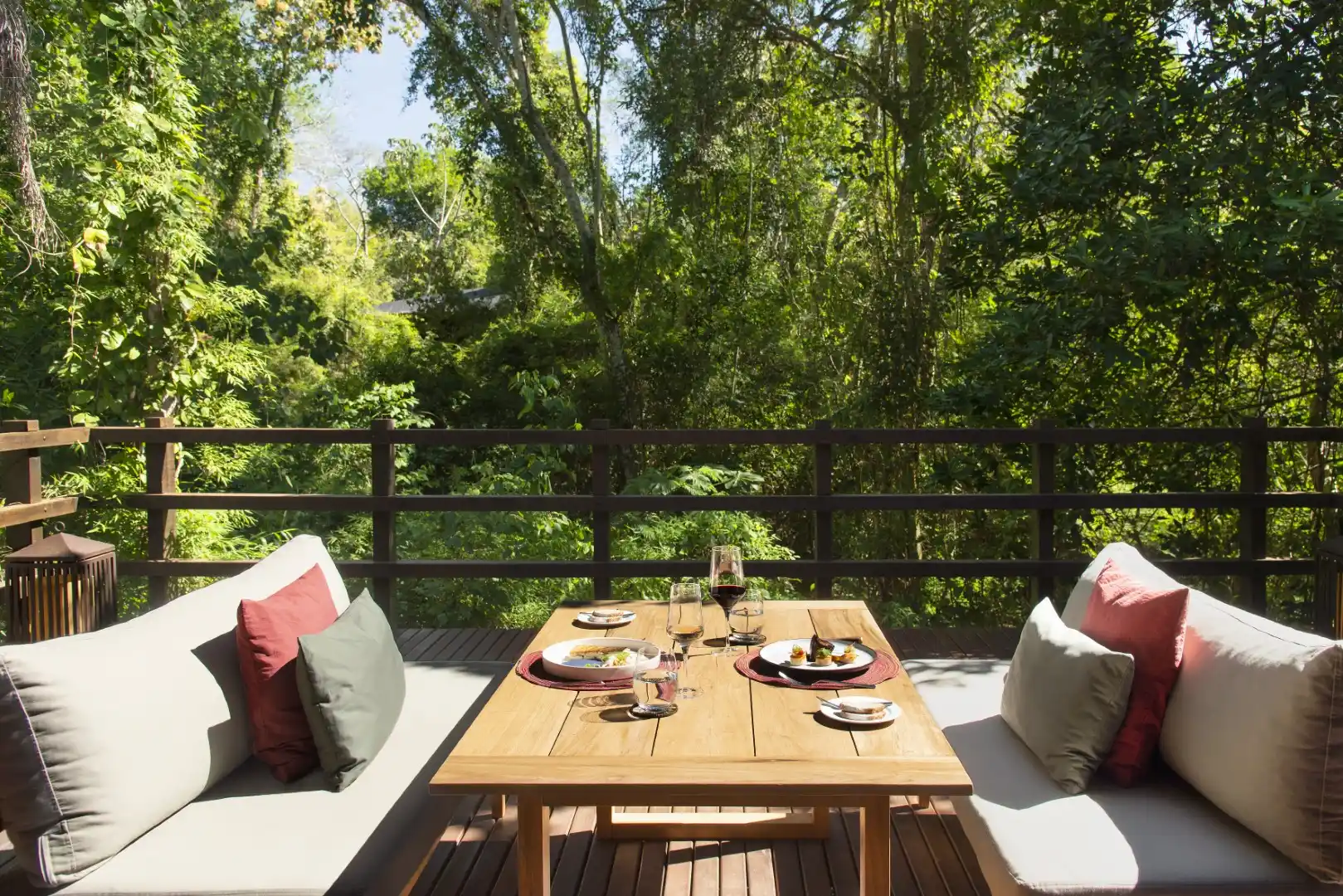 Outdoor dining setup on a wooden terrace surrounded by lush forest with table set for a relaxing meal