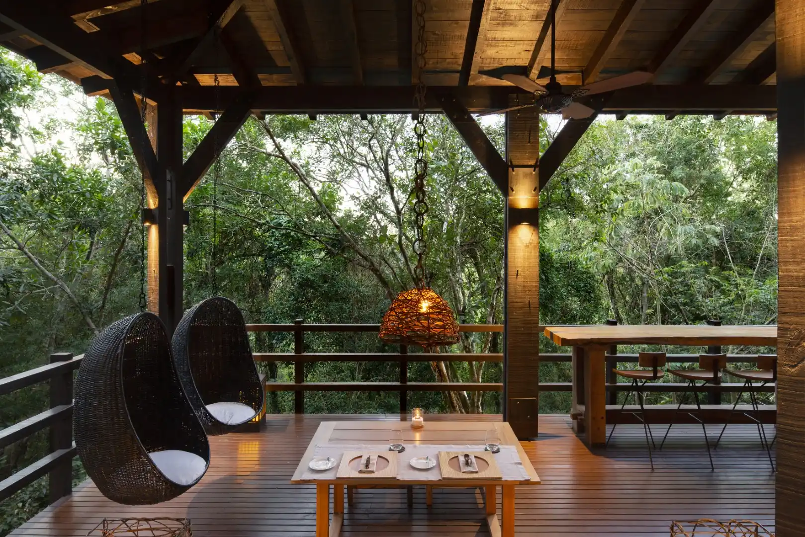 Covered wooden terrace with dining table hanging chairs and forest view creating a peaceful outdoor setting